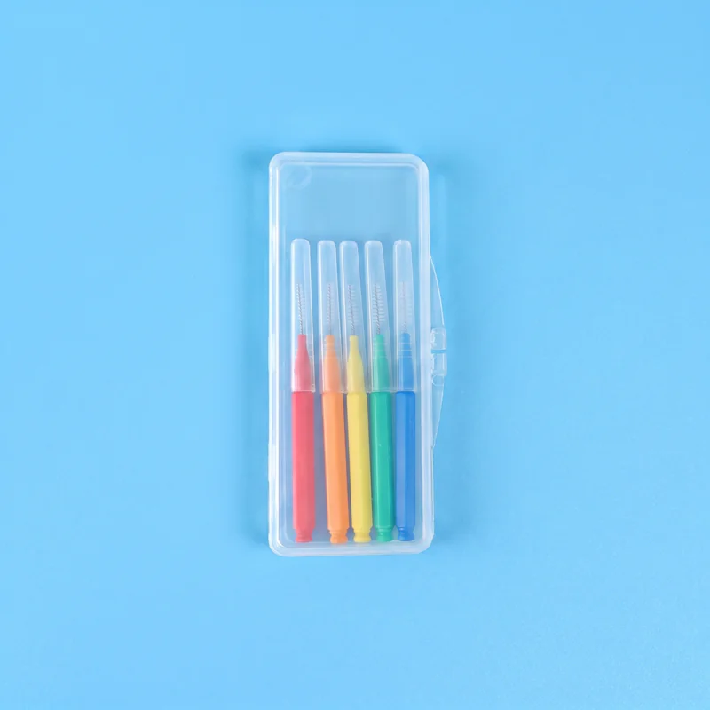 Five assorted color straight I-type interdental brushes packed inside small transparent plastic storage case on solid light blue background
