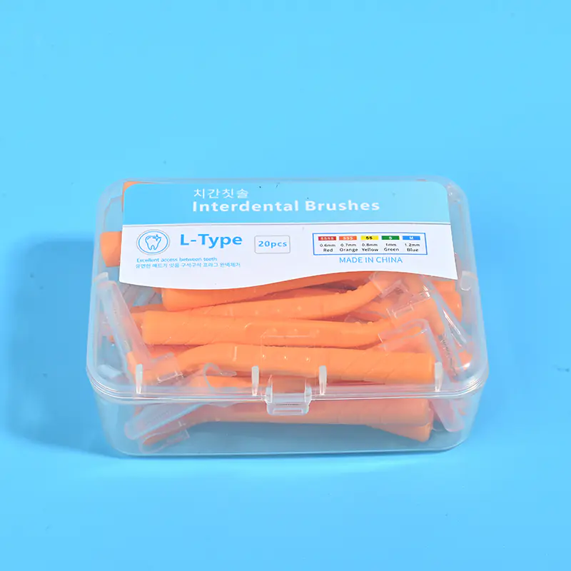 Close-up transparent plastic box filled with orange L-type interdental brushes, bilingual Korean English label with full ISO size color chart on solid light blue background