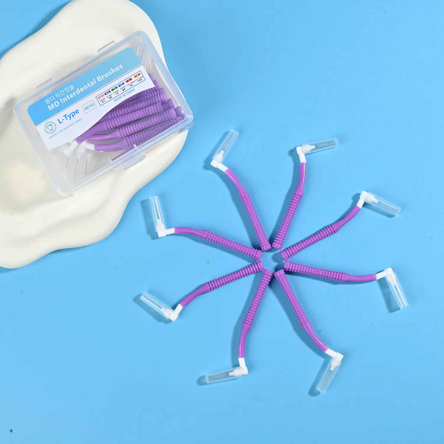 Purple L-type MD interdental cleaners arranged radial star shape with original clear storage box on beige irregular pad and bright blue background