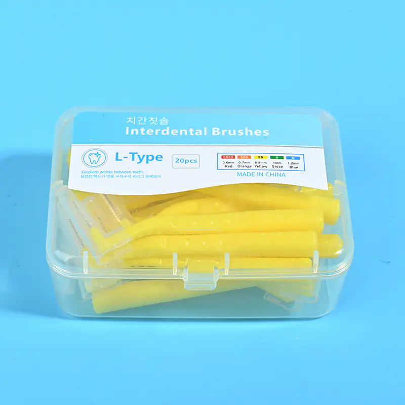 1-yellow-l-type-interdental-brush-20pcs-clear-box-closeup-blue-bg.jpg Close-up transparent plastic box filled with yellow L-type interdental brushes, bilingual Korean English label with full ISO size color specification chart on solid light blue background