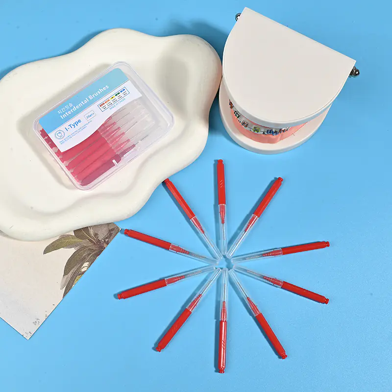 Red straight I-type interdental brushes arranged radial star shape with clear storage box and orthodontic dental model on beige irregular pad and blue background